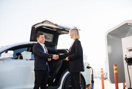Image of a man and woman shaking hands alongside a parked electric vehicle
